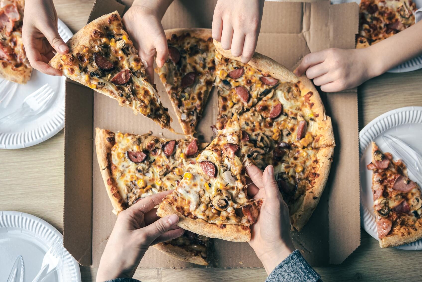 Jovenes tomando porciones de pizza caliente de una caja de carton en la vista superior de la mesa